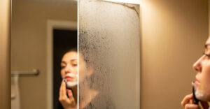 Frau rasiert sich vor einem beschlagenen Spiegel.